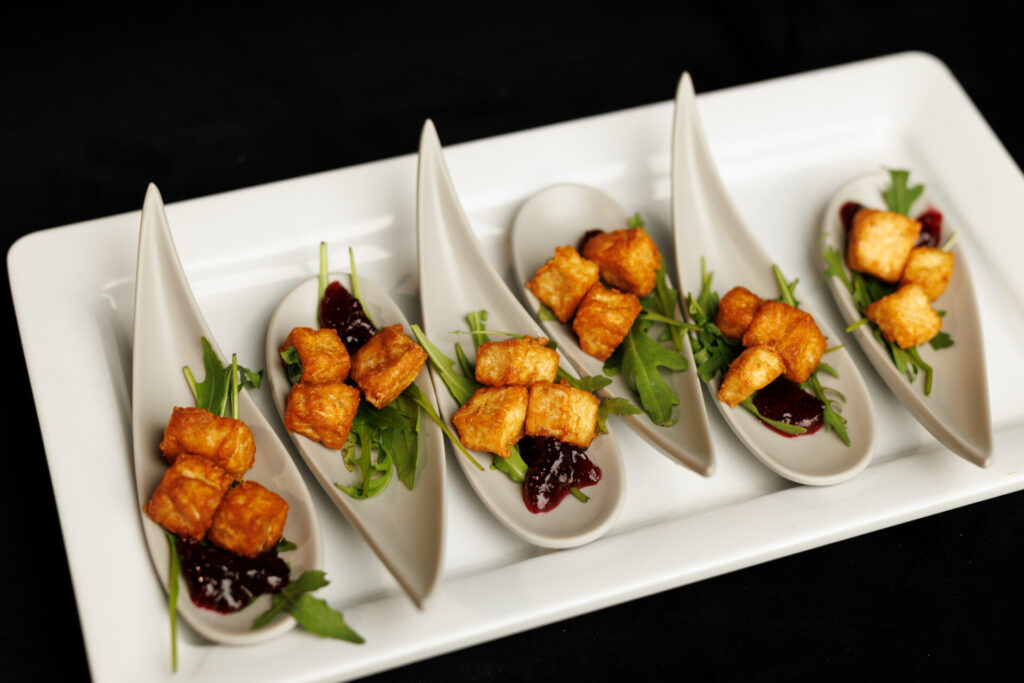 Crispy golden tofu cubes served on individual ceramic tasting spoons with a dollop of red berry jam and fresh arugula.