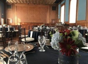 Elegant Winston-Salem party venue with a grand hall featuring round tables dressed in blue tablecloths and floral centerpieces, complemented by wooden paneling.