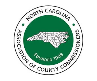 Logo of the North Carolina Association of County Commissioners. It features a green circle with a white map of North Carolina counties and text stating "Founded 1908" in the center.