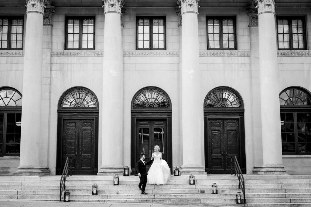 A wedding couple on the steps of the historic Millennium Event Center with soaring columns in the background.
